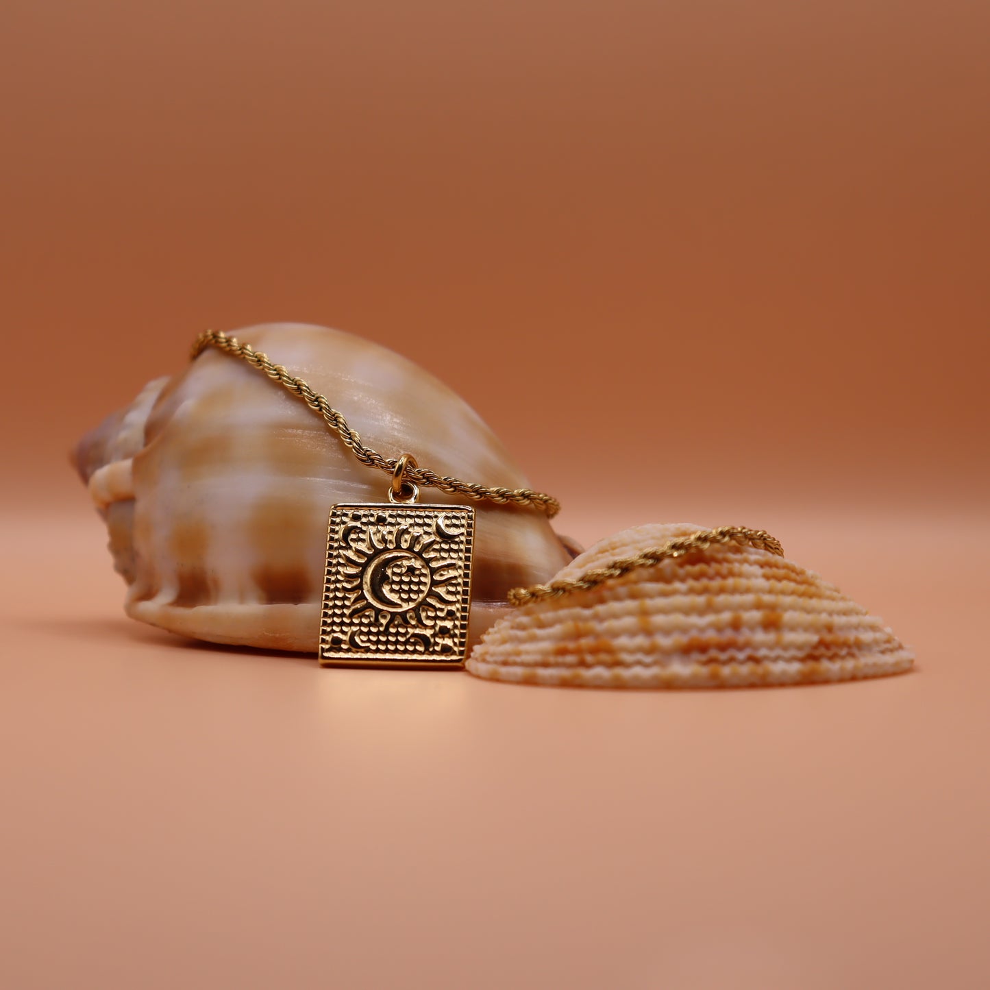 Gold necklace with a decorative pendant on a peach background with seashells.