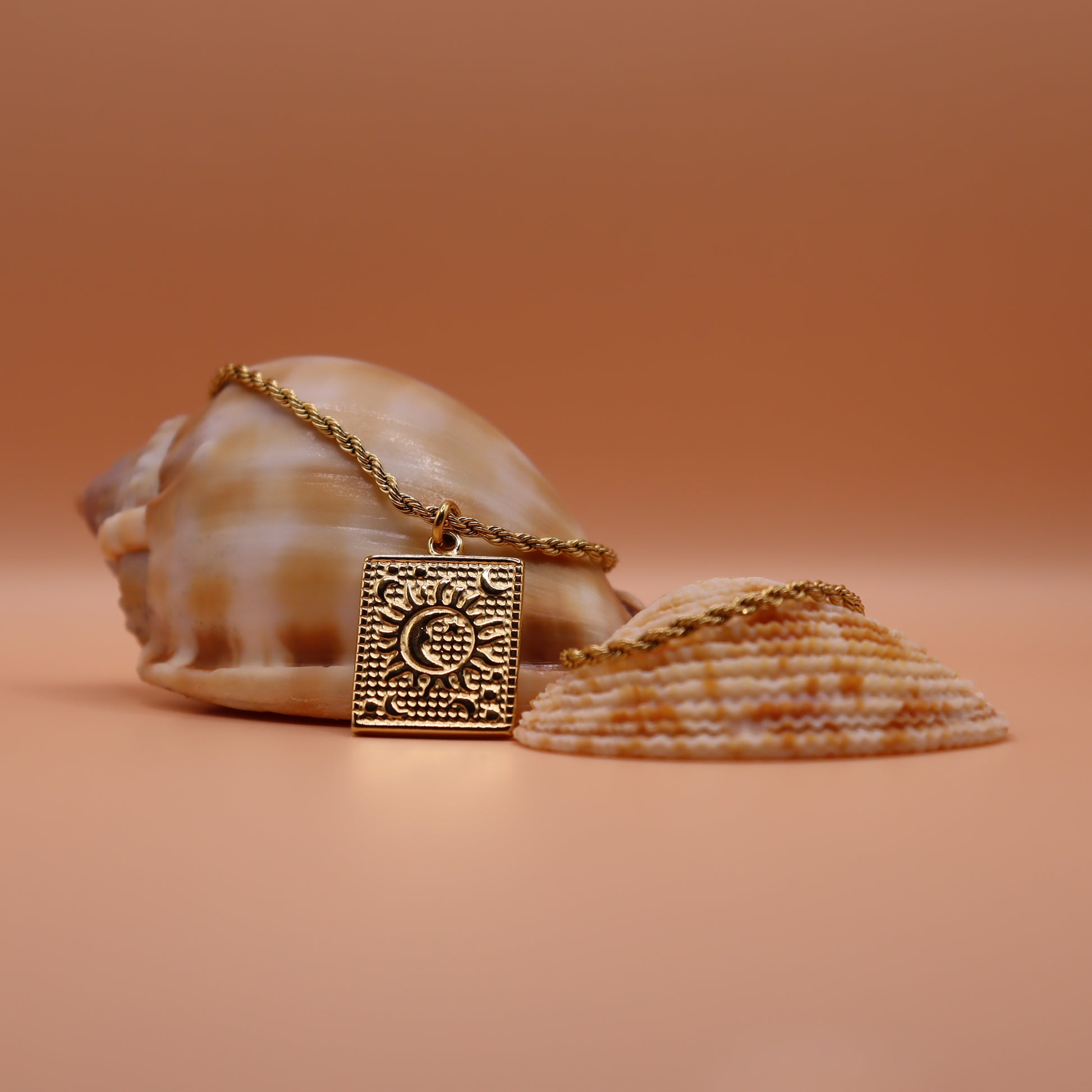 Gold necklace with a decorative pendant on a peach background with seashells.