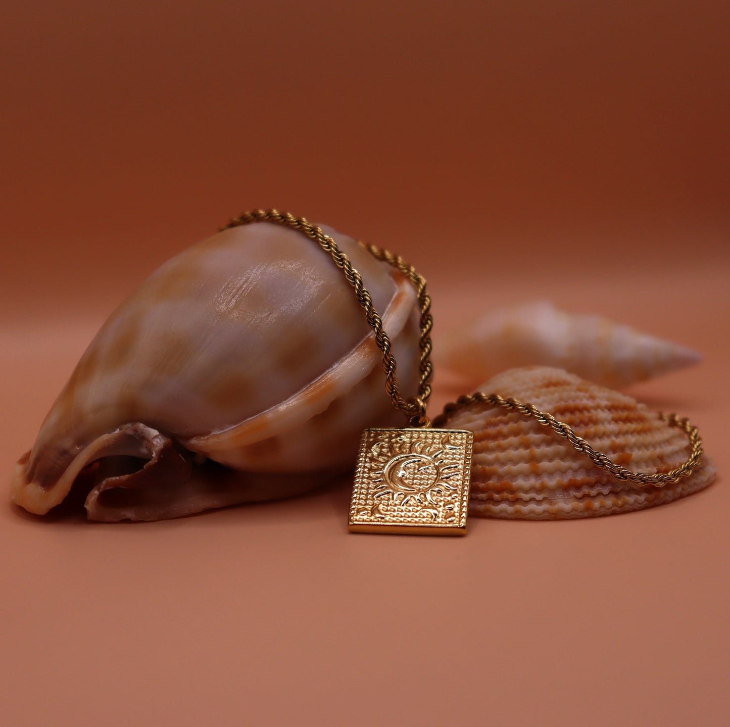 Gold necklace with a square pendant on a brown background with shells.