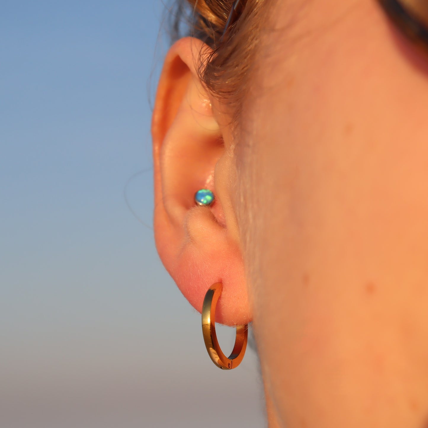 Close-up of an ear with a gold hoop earring against a blurred background