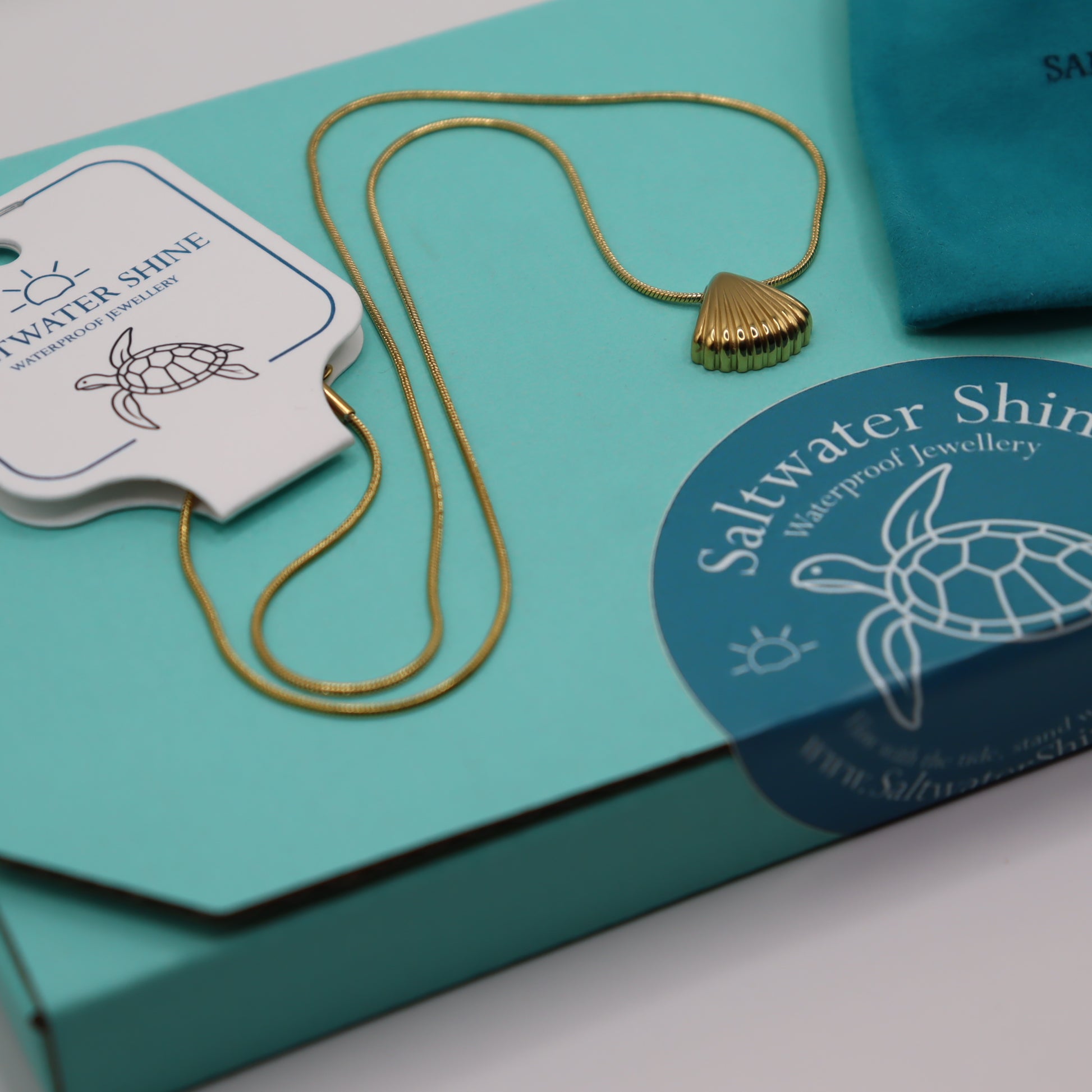 Gold necklace on a turquoise box with 'Saltwater Shine' branding.