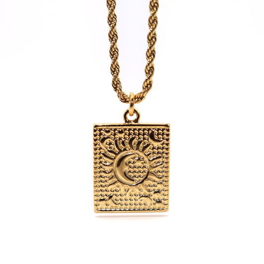 Gold necklace with a square pendant featuring sun and moon designs on a white background
