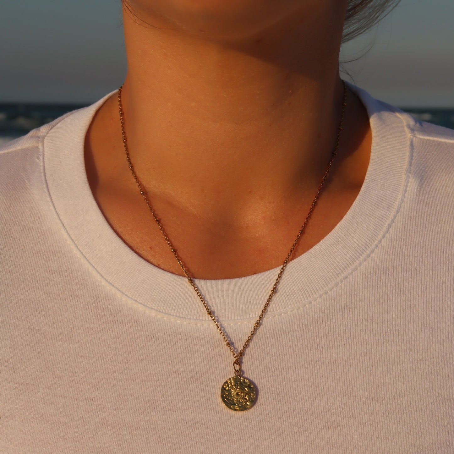 Necklace with a pendant worn by a person against a blurred natural beach background