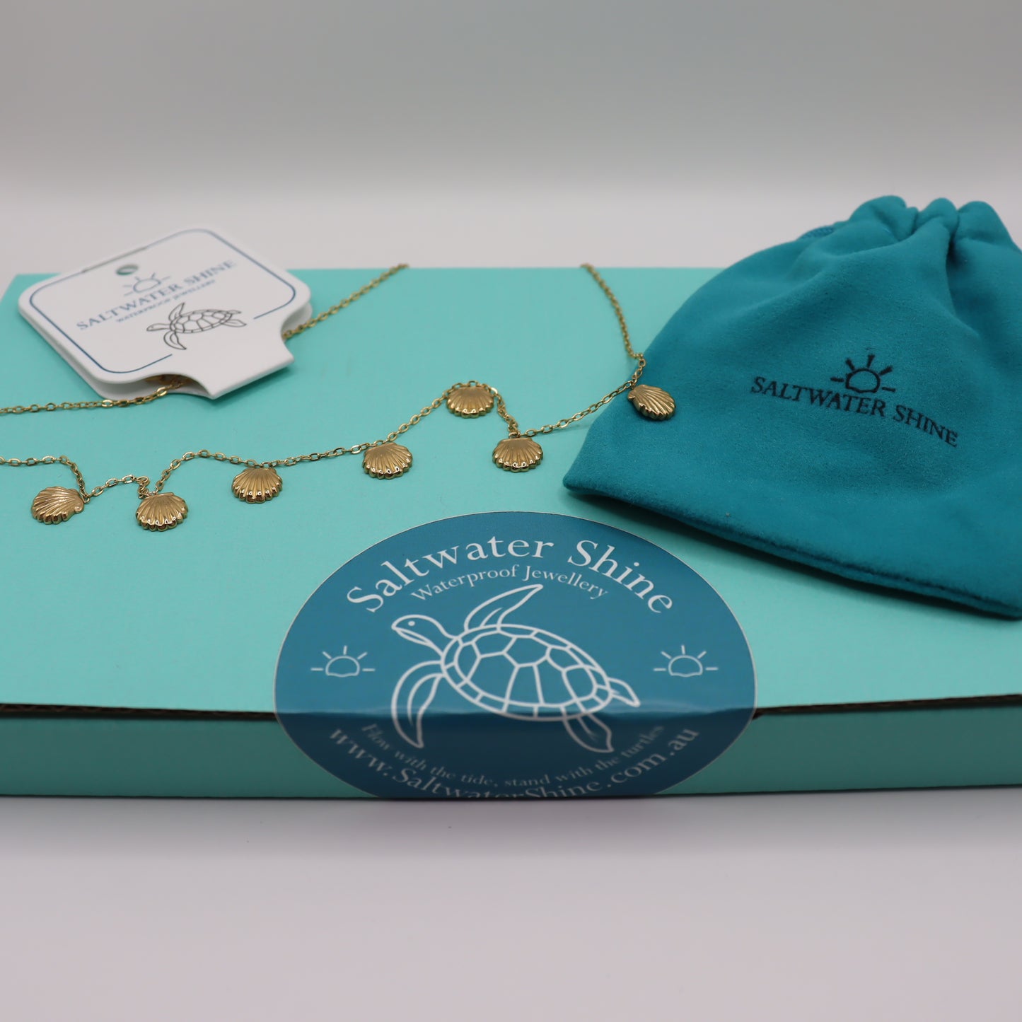 Gold 7 shell necklace on a 'Saltwater Shine' branded box with packaging and a turtle logo.