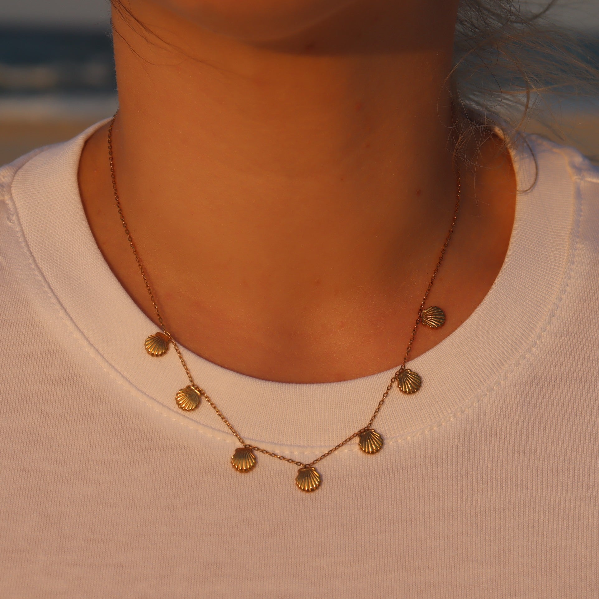woman wearing necklace with 7 shell pendants, at sunset