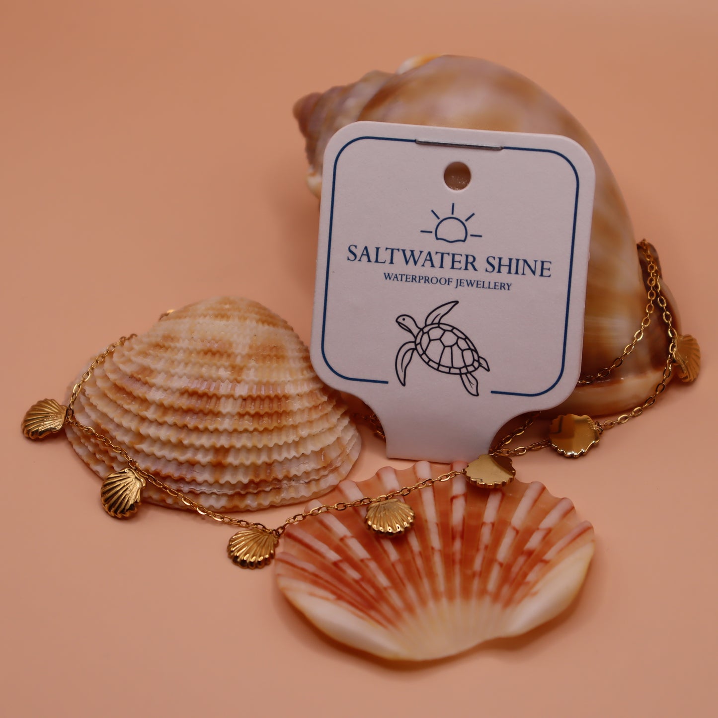 Gold necklace with shell pendants on a peach background with 'Saltwater Shine' jewelry tag.
