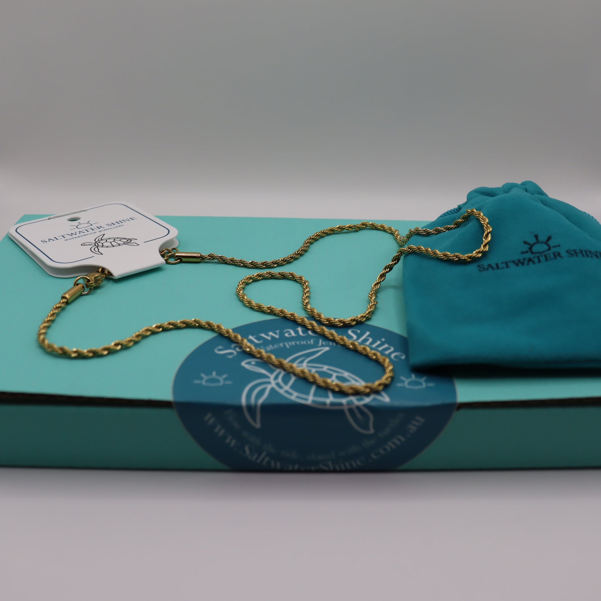 Gold chain necklace on a teal box with 'Saltwater Shine' branding