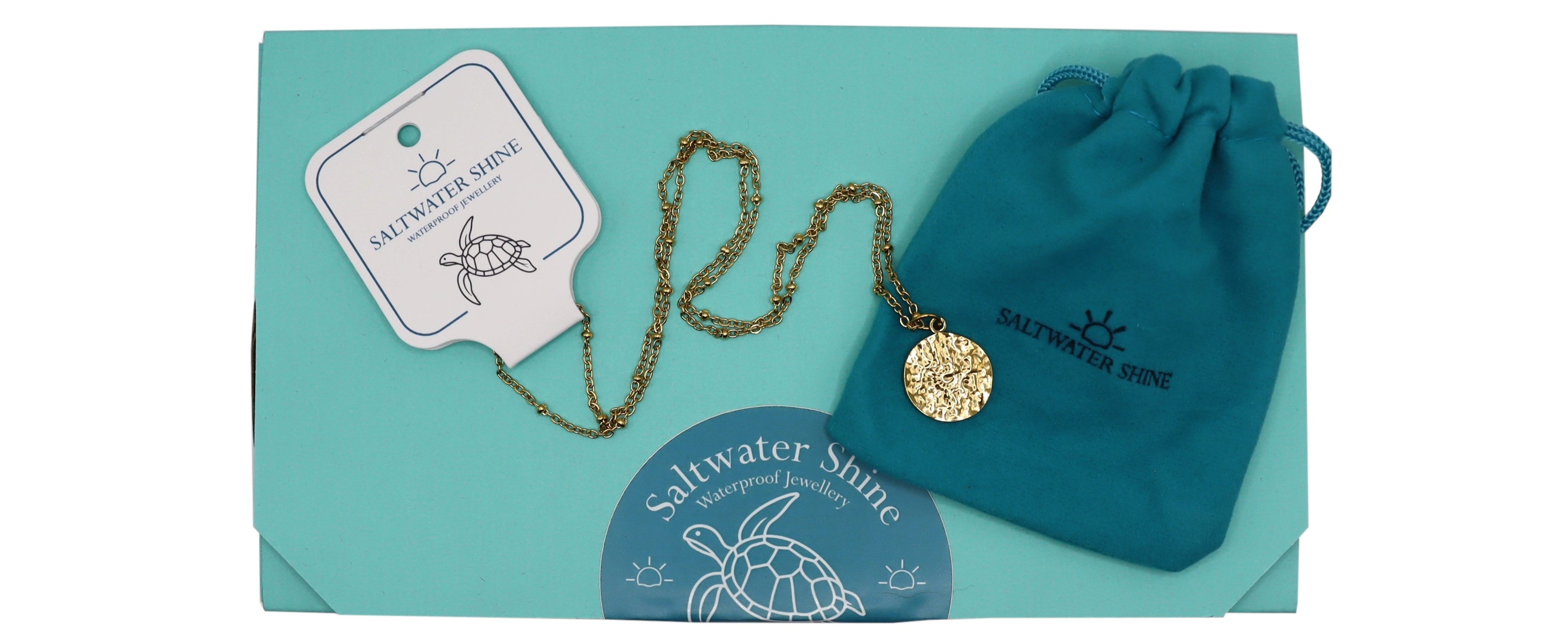 Gold necklace with a pendant on a teal background box, featuring 'Saltwater Shine' branding.