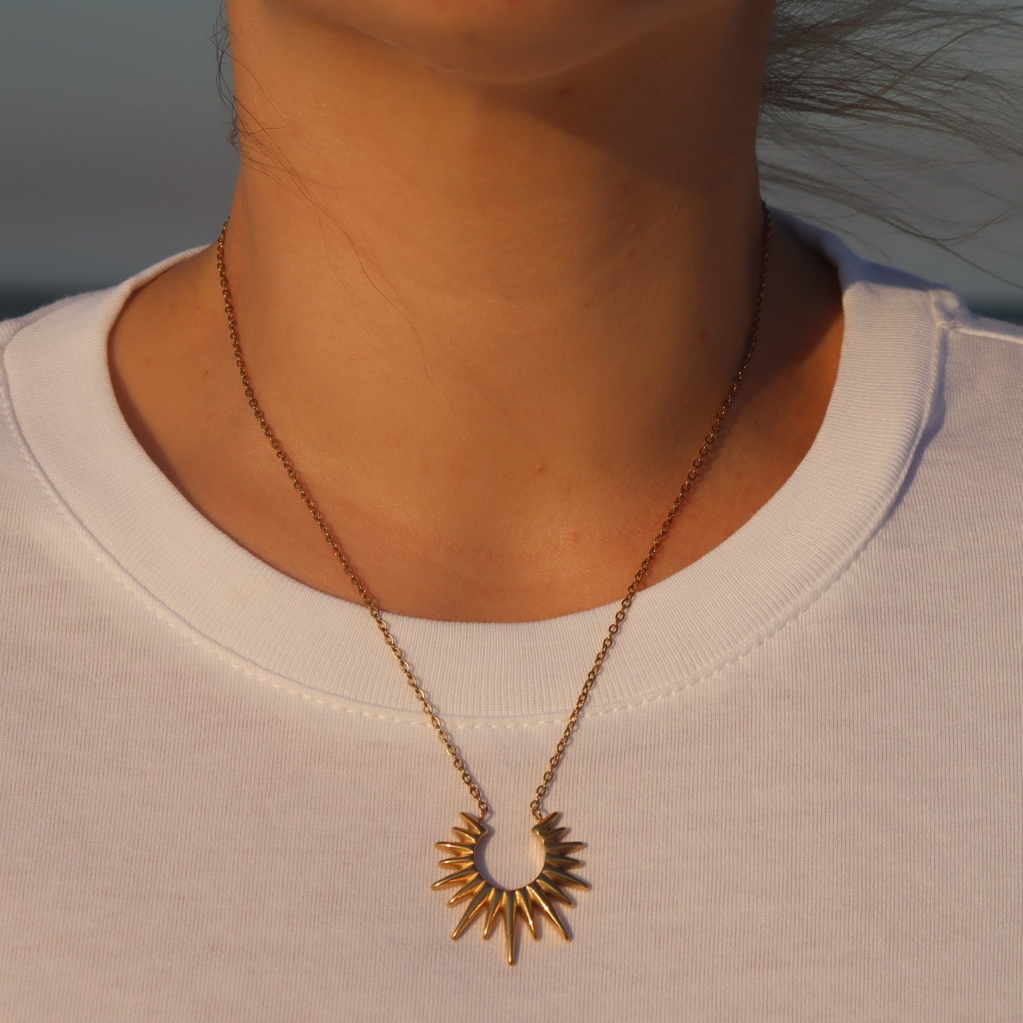 Gold necklace with a sunburst pendant worn by a person at a gold coast beach