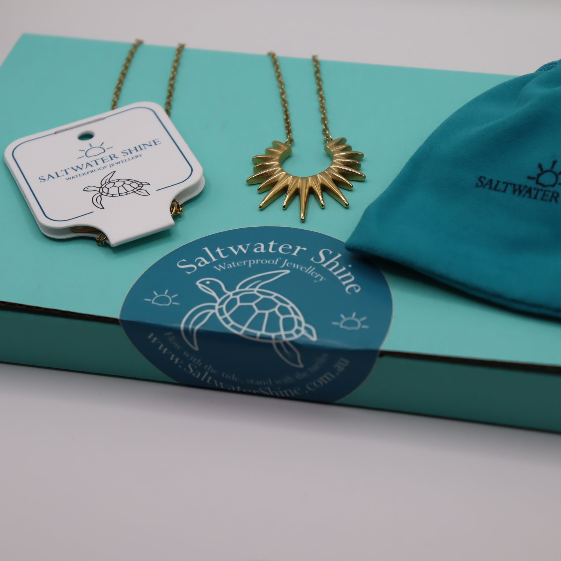 Gold necklace with 'Saltwater Shine' branding on a teal box.