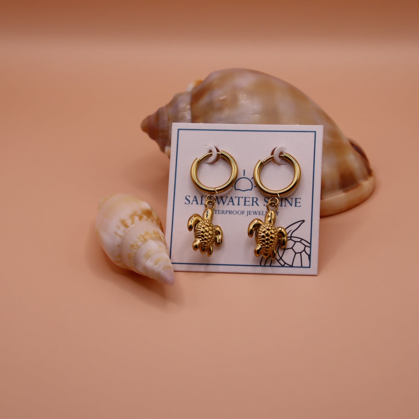 Gold turtle earrings on a card with seashells in the background