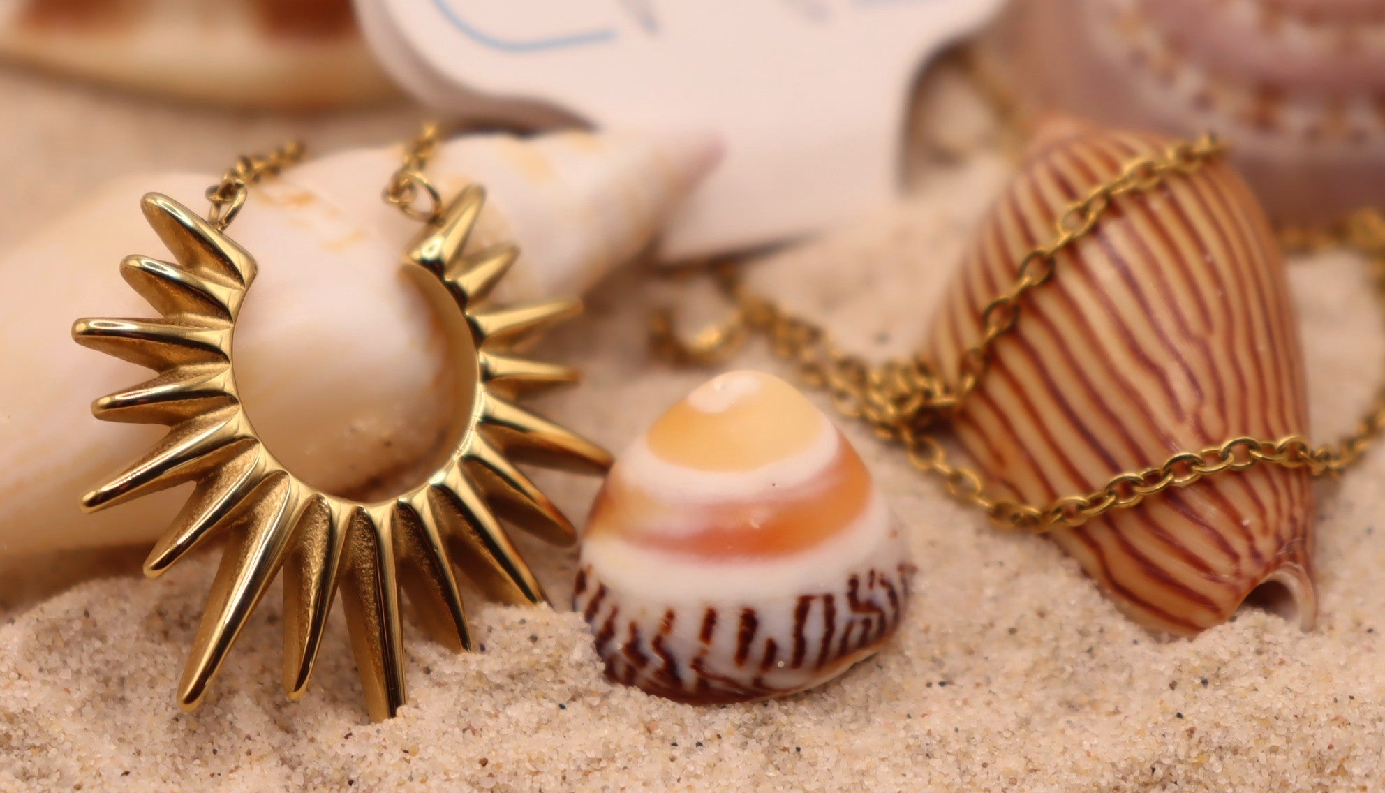 Gold sun-shaped pendant necklace on sand with seashells